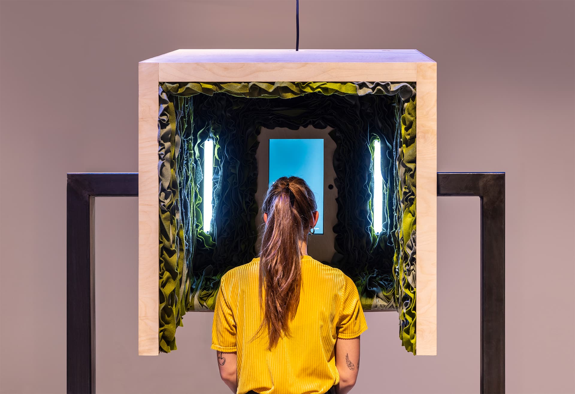 A woman is sitting inside one of the objects of the Channels installation. She looks at a screen that shows instructions.